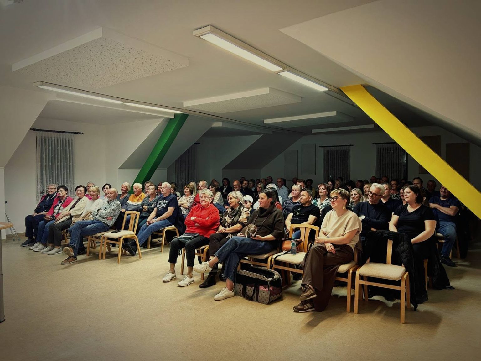 Zuschauer in einem Gemeindesaal mit Stühlen und einer Bühne